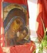 La stessa icona della Madonna con il Bambino esposta tra drappi rossi, con una pianta in primo piano