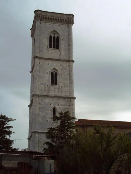 Il campanile di Orentano, alta torre in pietra chiara coronata da una cornice, con finestre ad arco su più ordini, sotto un cielo nuvoloso