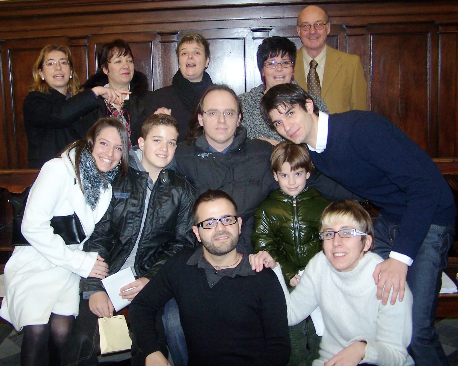 Coristi del coro parrocchiale, adulti e ragazzi, in posa sorridenti davanti agli stalli in legno del coro della chiesa