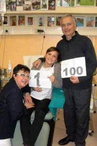 Un donatore con il cartello «100» accanto a una giovane seduta sulla poltrona per la donazione con il cartello «1», insieme a una donna accovacciata