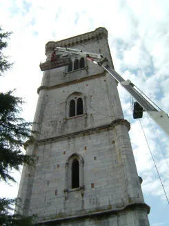 Il campanile in pietra di Orentano visto dal basso durante i lavori di restauro, con il braccio di una piattaforma mobile accostato alla sommità