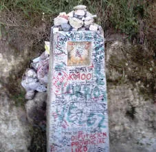 Cippo del Cammino coperto di scritte dei pellegrini e sormontato da sassi, con l'indicazione dei 100 km