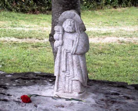 Statuetta in pietra di san Giacomo pellegrino con bastone e cappello, con una rosa rossa ai piedi