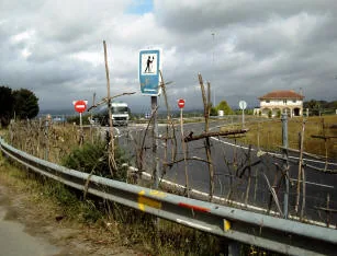 Rete lungo il bordo della strada piena di piccole croci fatte di rametti, sotto un cartello del Cammino