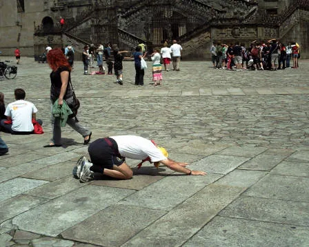 Un pellegrino inginocchiato bacia il selciato della piazza davanti alla cattedrale, tra altri pellegrini