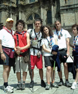 Sei pellegrini con fazzolettoni scout, zaini e bastoni in posa davanti alla cattedrale di Santiago